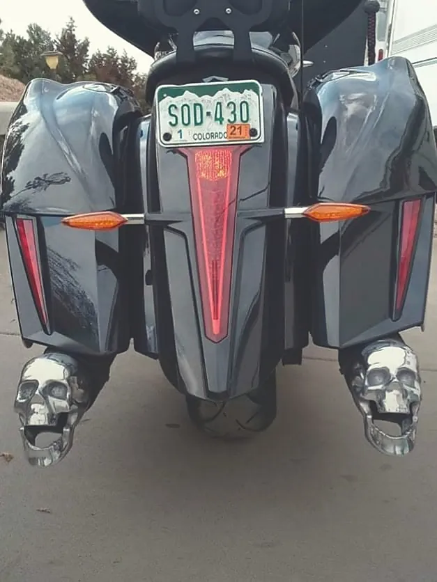 Polished chrome skull exhaust tips mounted on the dual exhaust of a black touring motorcycle