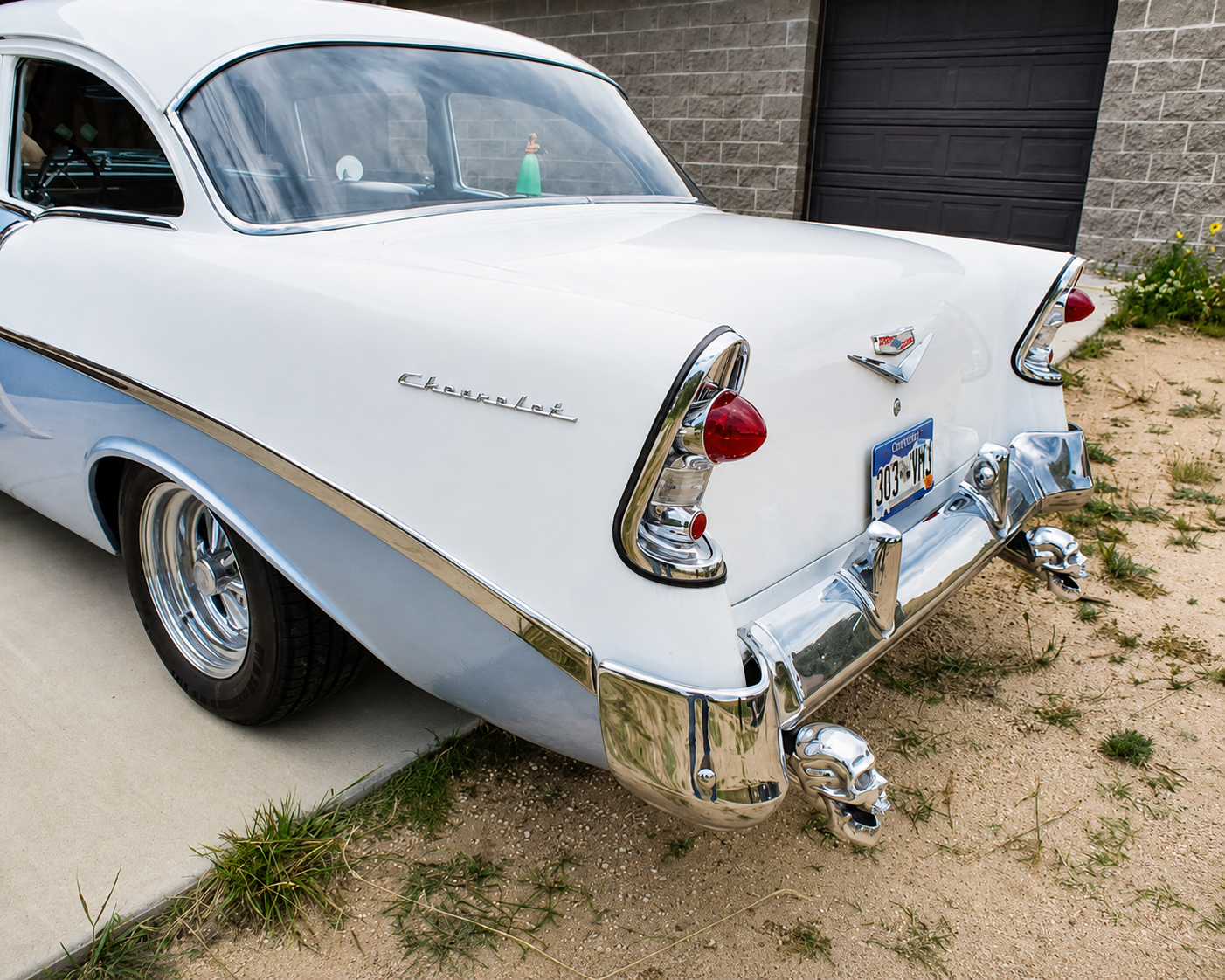Polished chrome skull exhaust tips installed under the rear bumper of a white 1956 Chevrolet