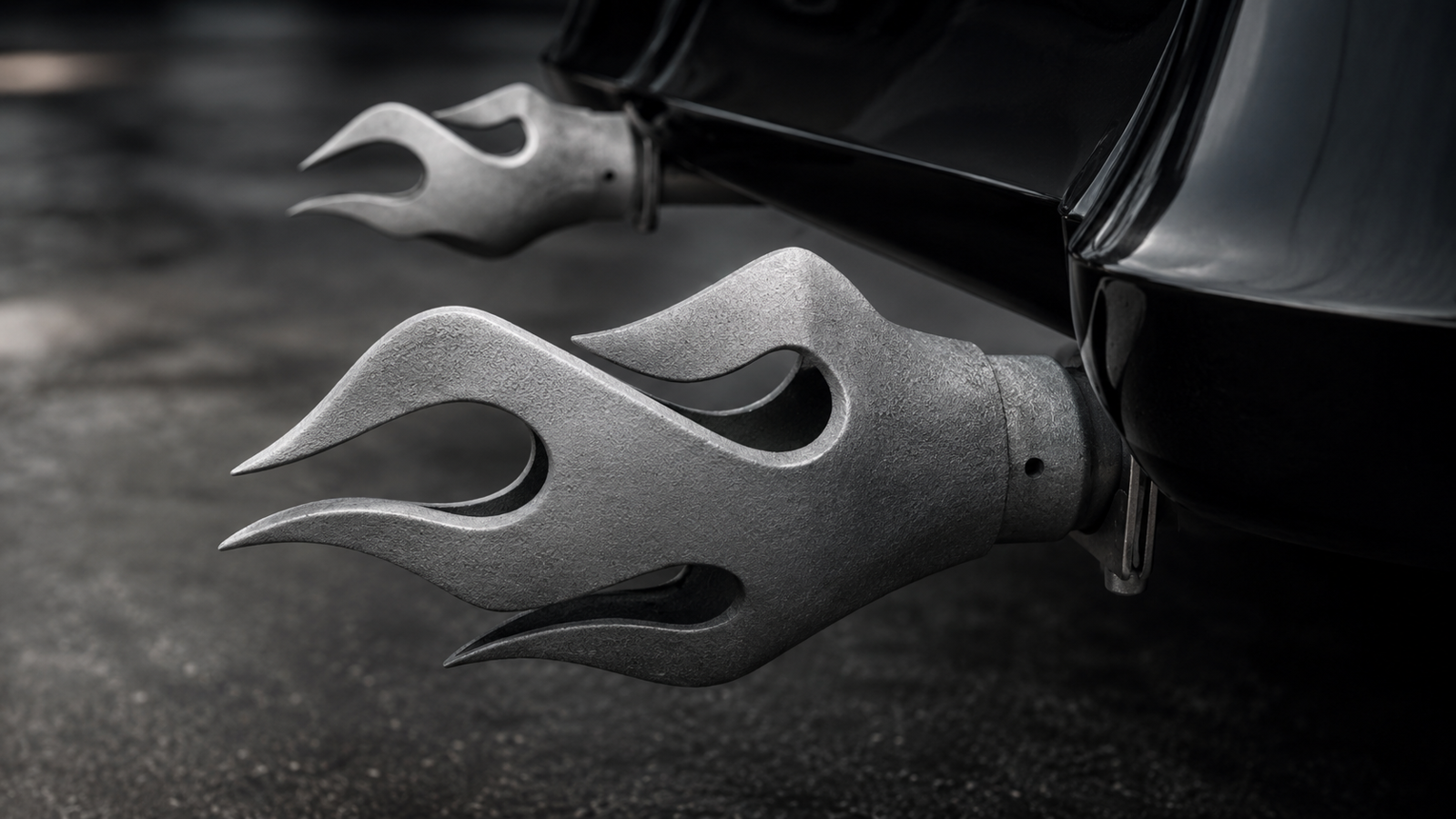 Dual flame-style exhaust tips in raw unpolished cast aluminum, mounted on the rear of a custom vehicle with a moody cinematic automotive look.